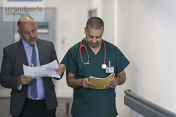Männlicher Verwaltungsangestellter und Chirurg lesen Papierkram im Krankenhausflur