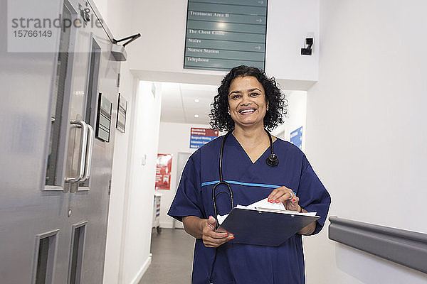 Porträt einer lächelnden  selbstbewussten Ärztin mit Krankenblatt bei der Visite im Krankenhausflur