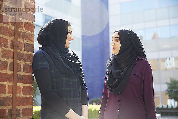 Junge Frauen in Hidschabs unterhalten sich vor einem sonnigen Gebäude
