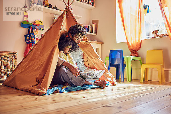 Vater und kleine Tochter lesen ein Buch im Tipi