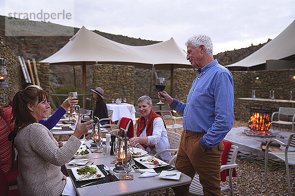 Älterer Mann mit Wein  der mit Freunden auf der Terrasse eines Restaurants anstößt