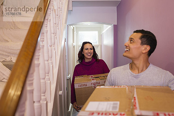 Glückliches Paar zieht in ein neues Haus ein und trägt Kartons durch den Flur