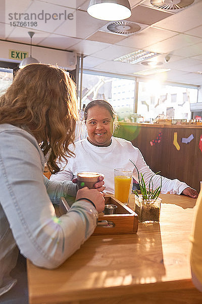 Junge Frau mit Down-Syndrom im Gespräch mit einem Freund in einem Cafe