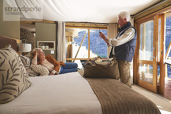 Älterer Mann mit Fotohandy  der seine Frau auf dem Hotelbett fotografiert