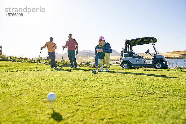 Männliche Golfer bereiten sich am sonnigen Abschlagplatz auf den Abschlag vor