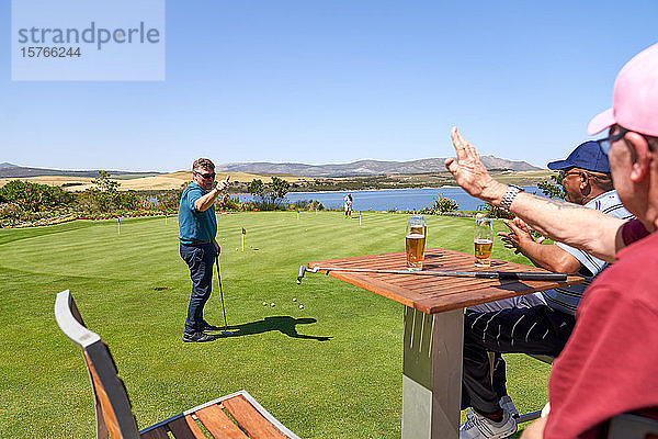 Männliche Golffreunde trinken Bier und üben Putten