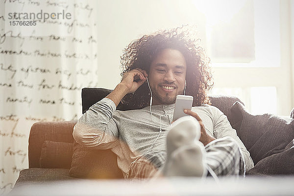 Junger Mann entspannt sich auf dem Sofa und hört Musik mit Kopfhörern und mp3-Player