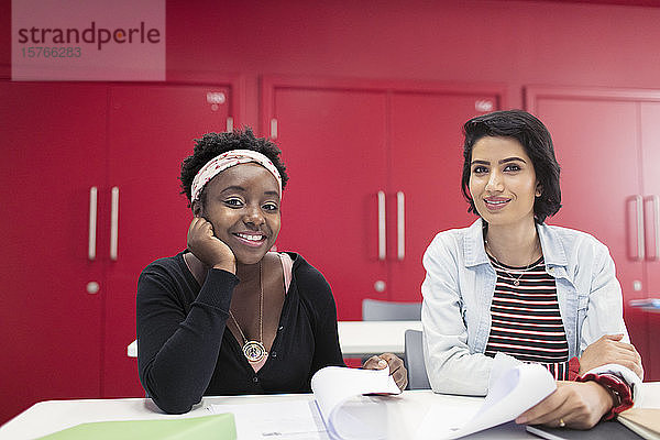 Porträt selbstbewusster  lächelnder weiblicher Community-College-Studenten mit Papierkram im Klassenzimmer