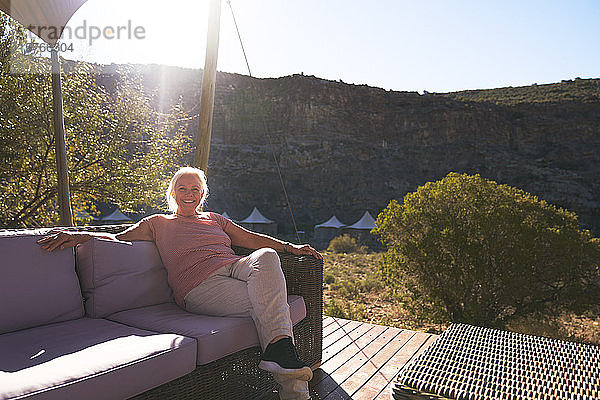 Sorglose ältere Frau entspannt sich auf dem sonnigen Balkon einer Safari-Lodge