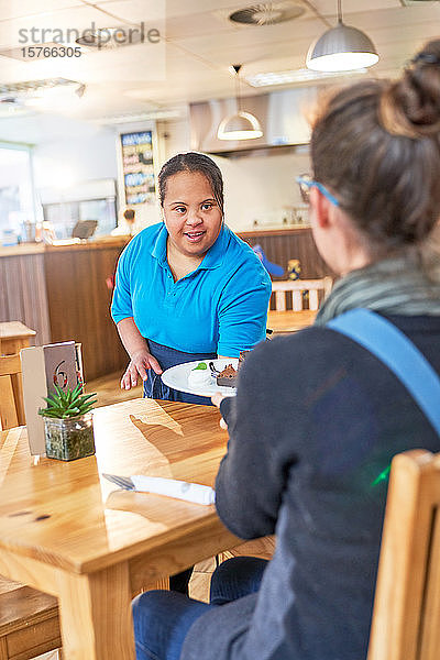 Junge Kellnerin mit Down-Syndrom serviert Essen in einem Cafe