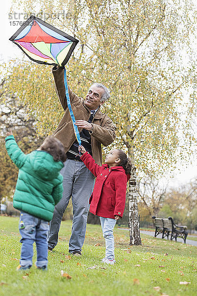 Großvater und Enkelkinder lassen im Herbst im Park einen Drachen steigen