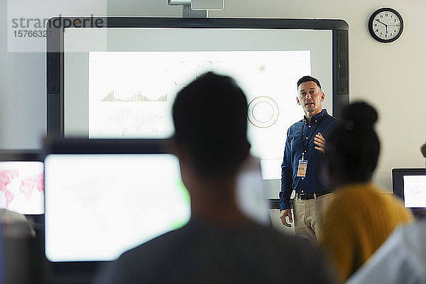 Männlicher Mittelschullehrer  der vor einer Projektionsfläche im Klassenzimmer Unterricht erteilt
