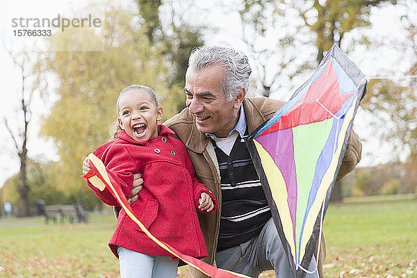 Verspielter Großvater und Enkelin lassen im Herbst im Park einen Drachen steigen