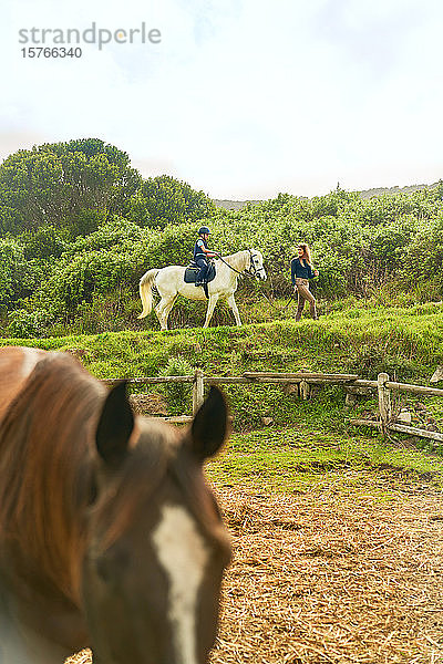 Frau führt Mädchen auf Pferd über ländliche Pferdekoppel