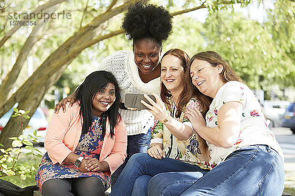 Glückliche Freundinnen benutzen ein Smartphone im Park