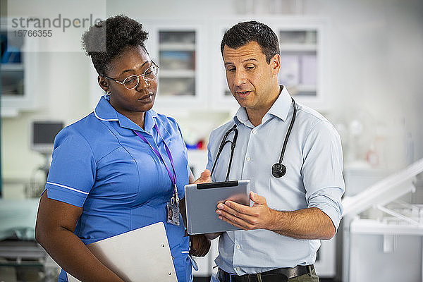 Männlicher Arzt mit digitalem Tablet im Gespräch mit einer Krankenschwester im Krankenhaus