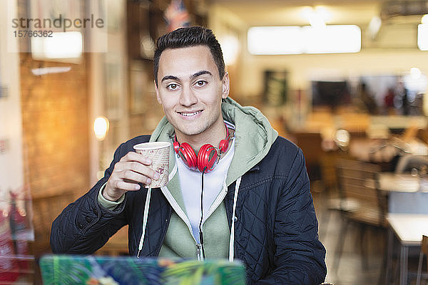 Porträt eines lächelnden  zuversichtlichen jungen Studenten  der in einem Caféfenster Kaffee trinkt und lernt