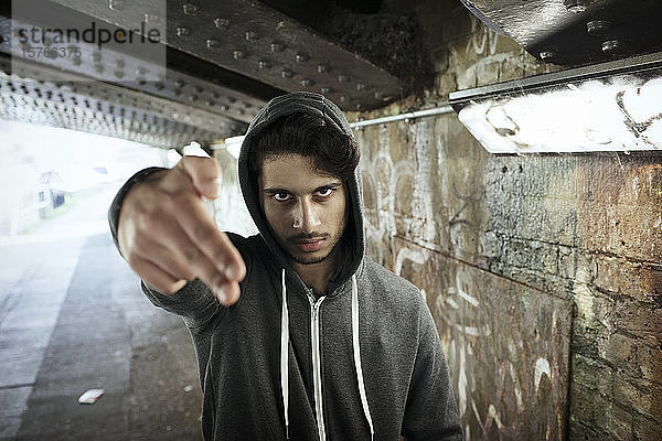 Porträt eines jungen Mannes  der in einem städtischen Tunnel mit dem Finger eine Pistole zeigt