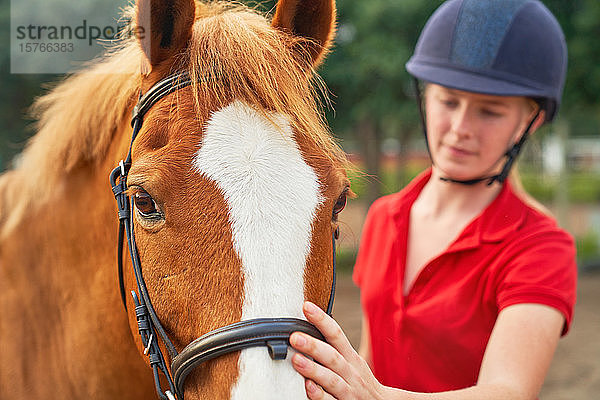 Teenager-Mädchen mit Reithelm streichelt Pferd