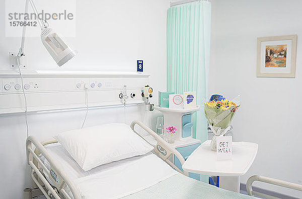 Blumenstrauß und Genesungskarte auf einem Tablett in einem leeren Krankenhauszimmer