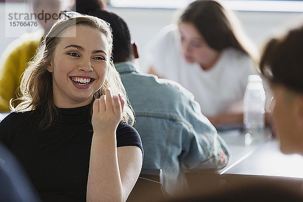 Glückliche  lächelnde High-School-Schülerin im Gespräch mit einem Klassenkameraden im Klassenzimmer
