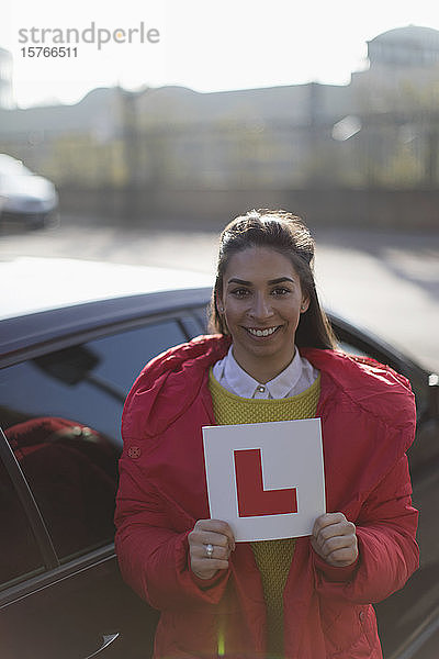 Porträt einer glücklichen jungen Frau  die einen Lernführerschein neben einem Auto hält