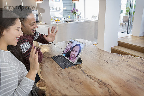 Glückliche Eltern führen Videokonferenzen mit ihren Töchtern am digitalen Tablet in der Küche durch
