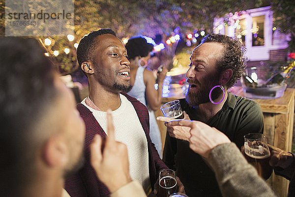 Glückliche männliche Freunde unterhalten sich und trinken auf einer Gartenparty