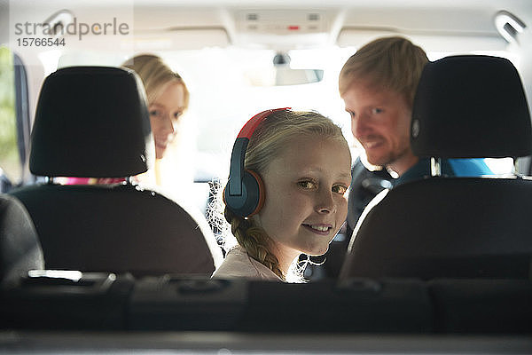 Portrait lächelndes Mädchen mit Kopfhörern auf dem Rücksitz eines Autos