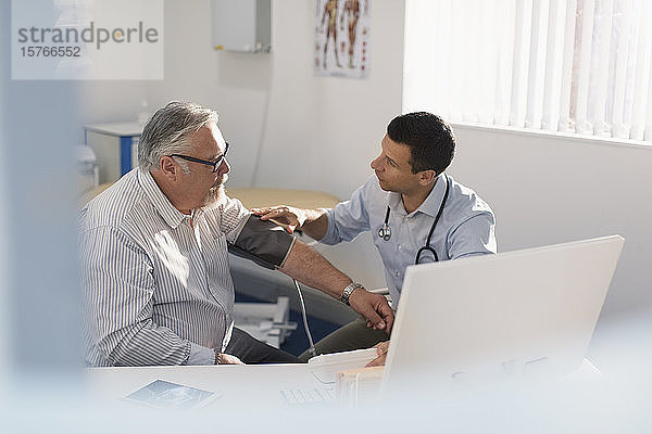 Männlicher Arzt prüft den Blutdruck eines älteren Patienten in einer Arztpraxis