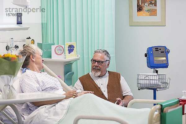 Zärtlicher älterer Mann  der seine Frau im Krankenhaus besucht und mit ihr spricht