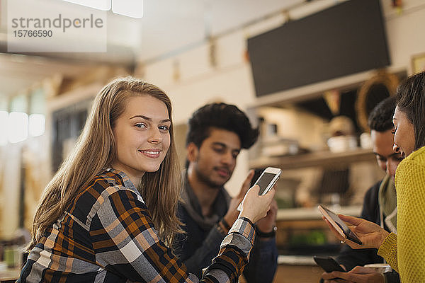 Porträt einer selbstbewussten jungen Frau  die in einem Café mit Freunden ein Smartphone benutzt