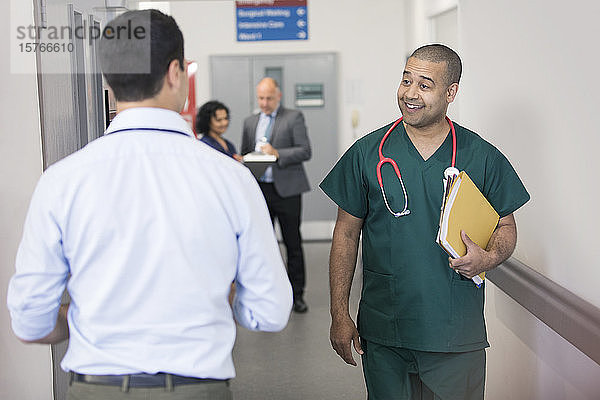 Lächelnder männlicher Chirurg  der einen vorbeigehenden Arzt im Krankenhausflur begrüßt