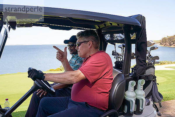 Männliche Golfer fahren Golfwagen auf einem Golfplatz am See