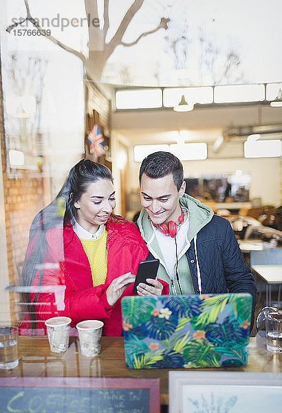 Junges Paar benutzt ein Smartphone am Fenster eines Cafés