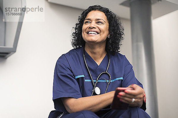 Porträt einer lächelnden  glücklichen Ärztin  die ein Smartphone benutzt