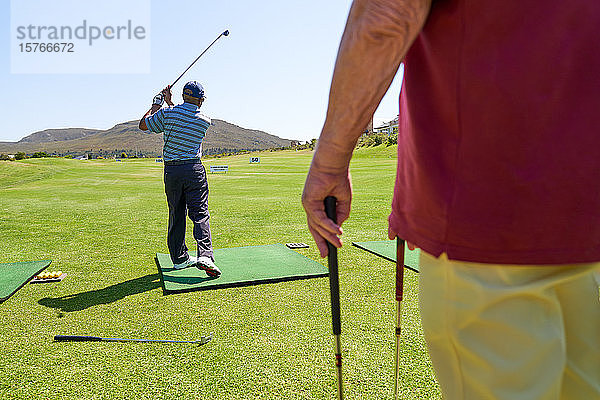 Männlicher Golfer beim Üben auf der Driving Range eines sonnigen Golfplatzes