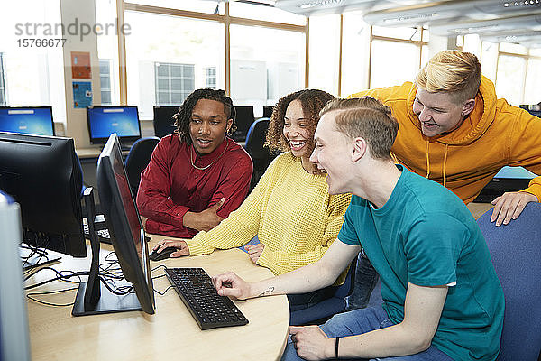 Glückliche junge Studenten  die gemeinsam einen Computer in der Bibliothek benutzen