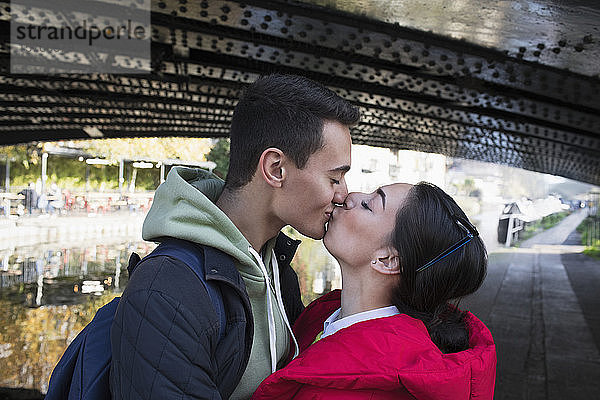 Zärtliches junges Paar  das sich unter einer Brücke küsst
