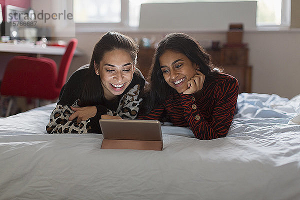 Glückliche Mädchen im Teenageralter benutzen ein digitales Tablet auf dem Bett