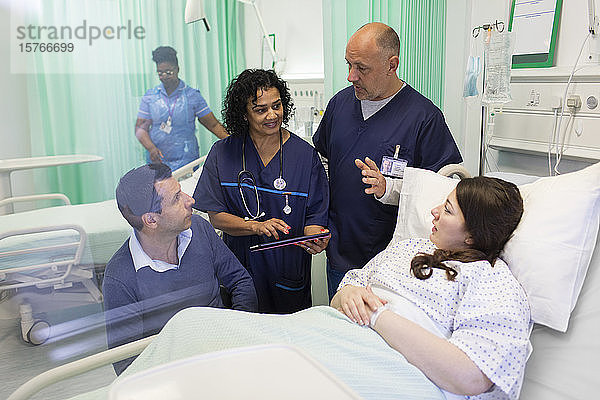 Ärzte mit digitalem Tablet bei der Visite  im Gespräch mit einem Paar auf der Krankenstation