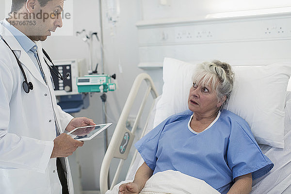 Arzt mit digitalem Tablet bei der Visite  Gespräch mit älterem Patienten im Krankenhausbett