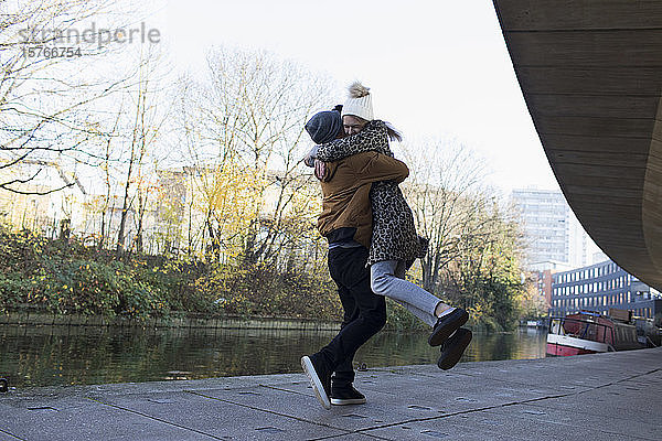 Glückliches junges Paar  das sich entlang eines städtischen Kanals umarmt