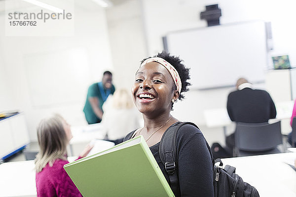 Porträt einer glücklichen  selbstbewussten Studentin mit Mappe im Klassenzimmer