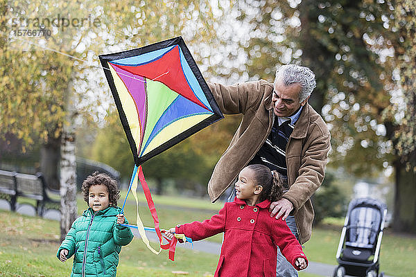 Großvater und Enkelkinder lassen im Herbst im Park einen Drachen steigen
