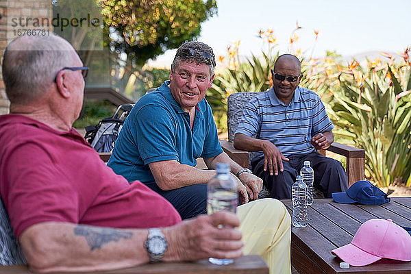 Ältere männliche Golffreunde unterhalten sich und trinken Wasser auf der Terrasse