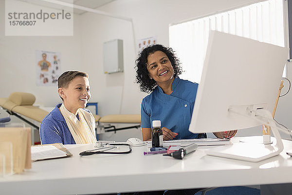 Weibliche Kinderärztin und Junge Patient im Gespräch  mit Computer in der Arztpraxis