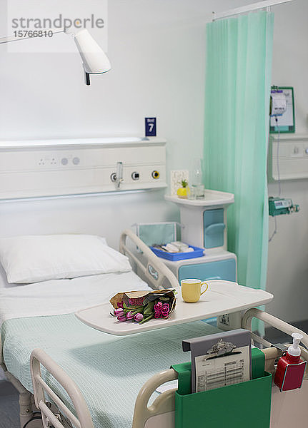 Blumen auf einem Tablett über einem Krankenhausbett in einem leeren Krankenhauszimmer