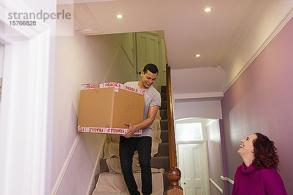 Glückliches Paar zieht aus dem Haus aus und trägt einen Karton die Treppe hinunter