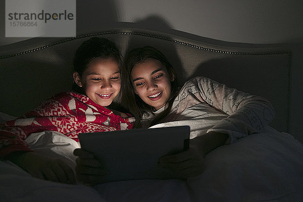 Mädchen schauen einen Film auf einem digitalen Tablet in einem dunklen Schlafzimmer